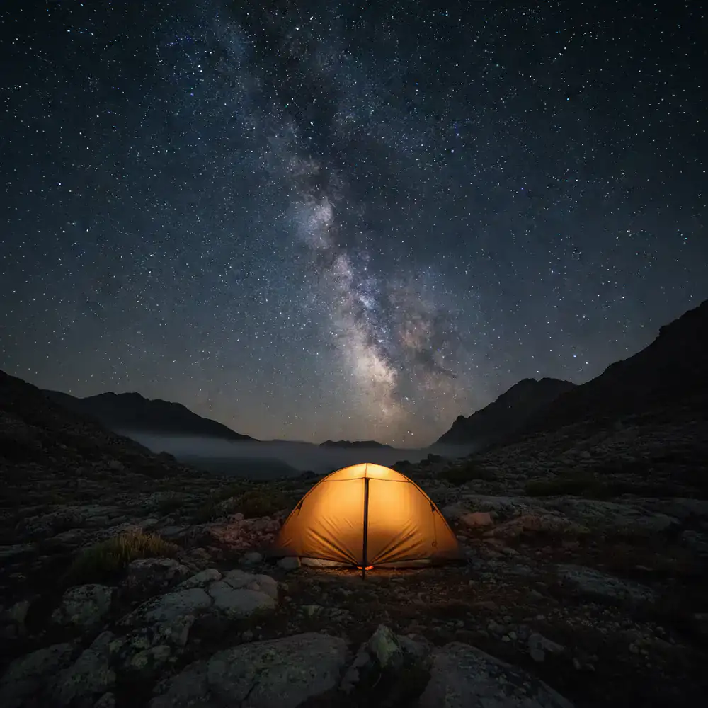 A glowing orange tent pitched under a vast starry sky at night